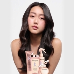 Kobieta z długimi, lśniącymi włosami, prezentująca efekty stosowania gamy Gloss Absolu. Na pierwszym planie produkty z linii, w tym Anti-Frizz Glaze Milk.