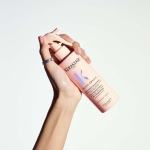 Dłoń trzymająca butelkę Kérastase Gloss Absolu Anti-Frizz Glaze Milk, prezentująca ergonomiczny design i wygodny aplikator produktu.