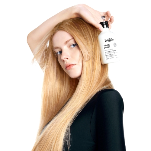 Modelka z długimi blond włosami trzymająca szampon L’Oréal Metal Detox