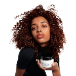 Modelka z kręconymi włosami trzymająca maskę L’Oréal Metal Detox