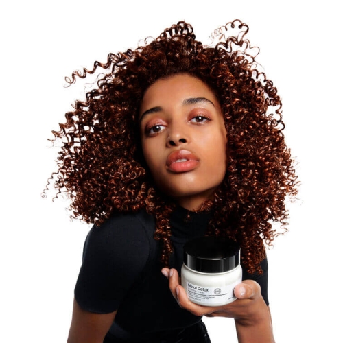 Modelka z kręconymi włosami trzymająca maskę L’Oréal Metal Detox